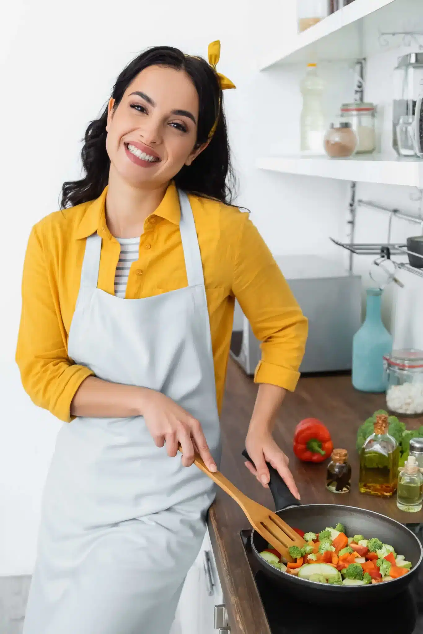Chef Maya Sterling smiling in a cozy kitchen, holding a wooden spoon near a stove with fresh ingredients on the counter.