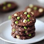 stack of chocolate pea cookies on wooden table with peas and chocolate pieces